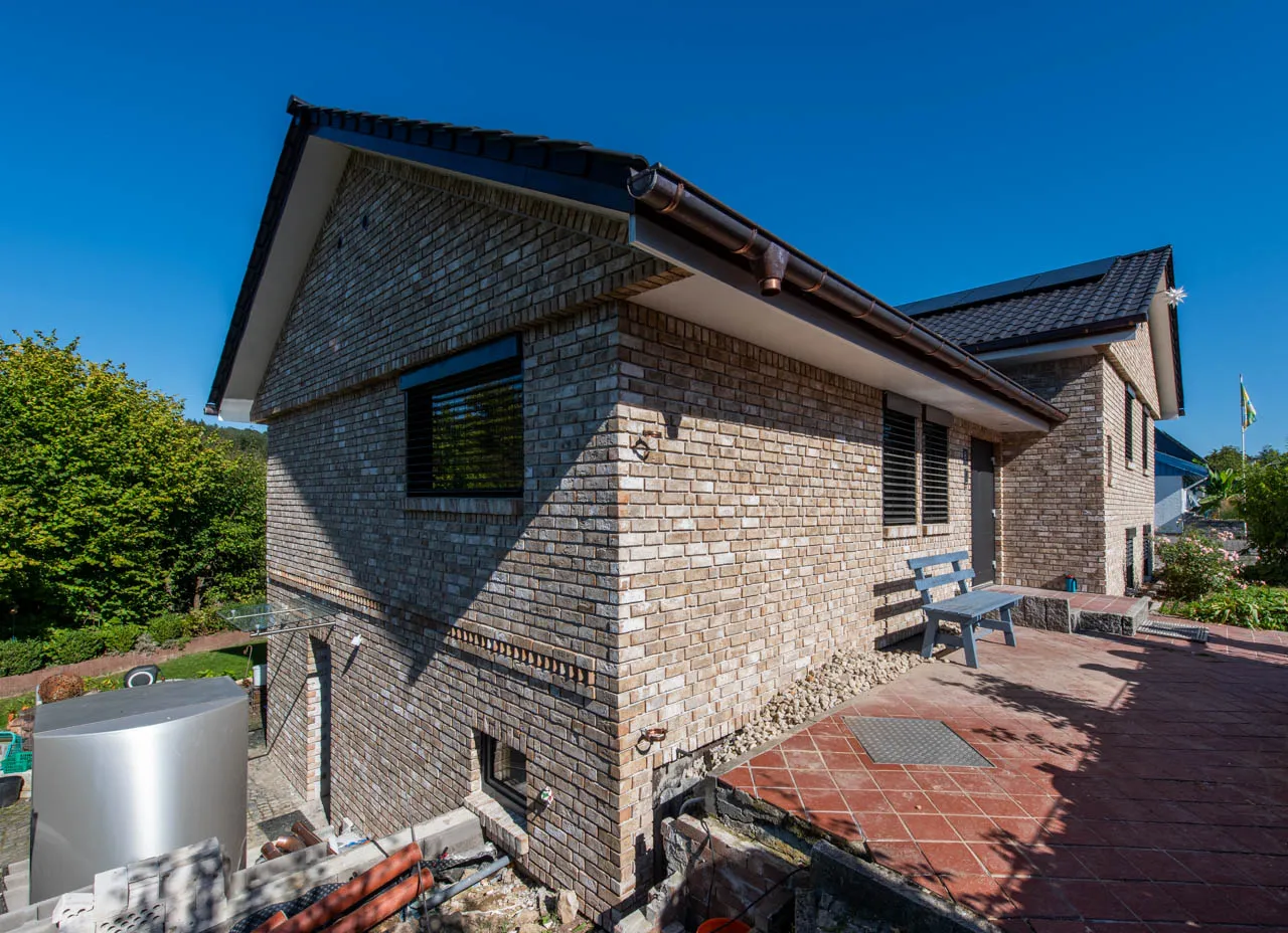 Modernes, helles Klinkerhaus mit dunklen Fenstern. Es werden durch halbe Steine tolle Akzente gesetzt. Die Sorte irish Moor mit seinen gelben, bronzenen Klinkerriemchen erstrahlen im Sonnenschein.